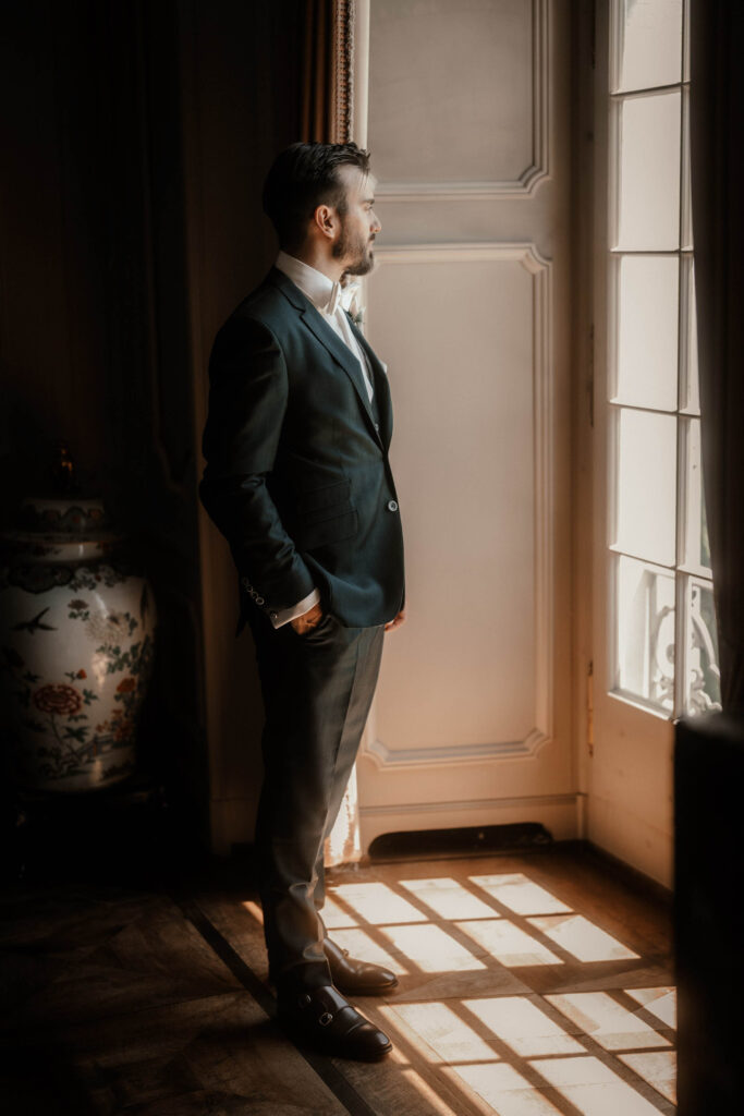 hochzeit-st-charles-hall-meggen-getting-ready-braeutigamm-steht-vor-altem-fenster